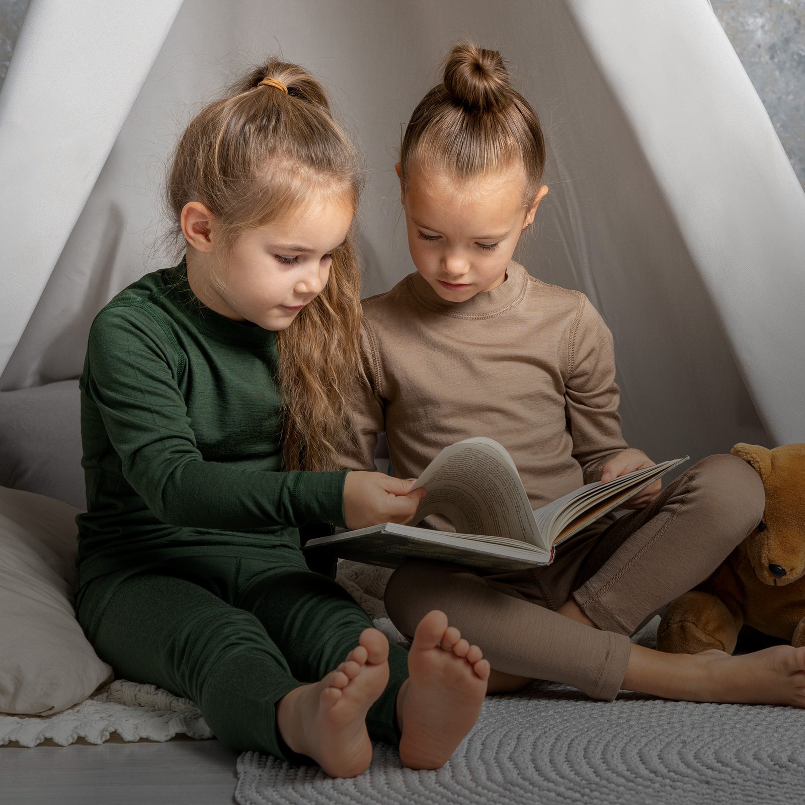Two children sitting inside a teepee reading a book.